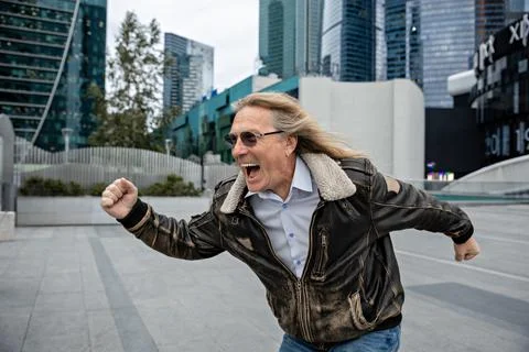 A middle-aged man in a jacket runs happily in the city center and shouts Stock Photos