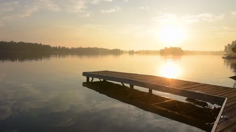 Middle aged man jumping off dock as sun rises in background.  Stock Footage 94175540