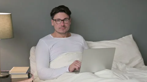 Middle Aged Man with Laptop Looking at Camera in Bed Stockbeeldmateriaal 142368829