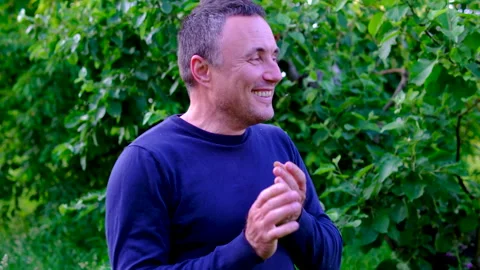 Middle aged man laughing sincerely and clapping hands with joy while enjoying Stock Footage 345747421