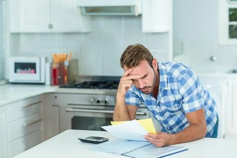 Middle-aged man leaning at kitchen island, holding papers, reviewing folder, Stock Photos