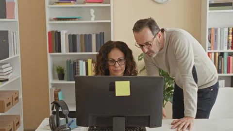 Middle aged man leans over seated woman at computer monitor in building, gu.. Stock Footage 337416017