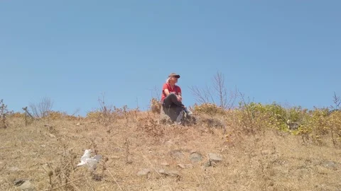 Middle-aged man with long gray hair, in dark glasses, sits resting on seashore Stock Footage 139440526