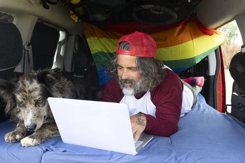 Middle-aged man lying in the camping van with his pet and using a laptop. A.. Stock-Fotos