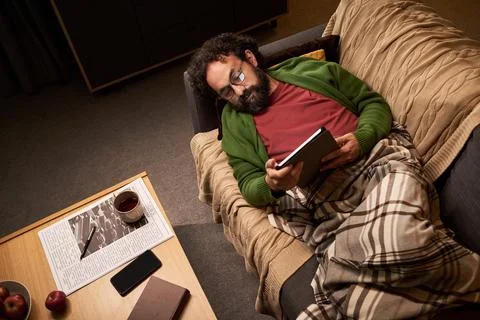 Middle Aged Man Lying on Couch and Reading on Ereader at Night Stock Photos