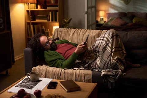 Middle Aged Man Lying on Sofa and Reading Ebook at Night Stock Photos