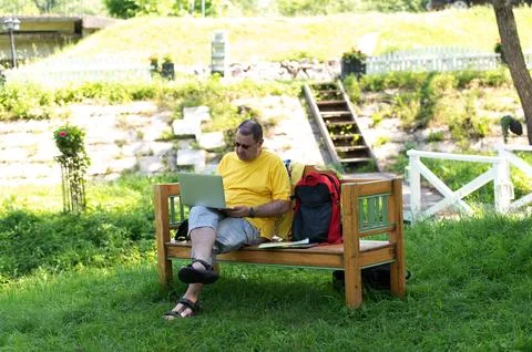 Middle-aged man man sitting on the wooden bench in park and using laptop, wor Stock Photos