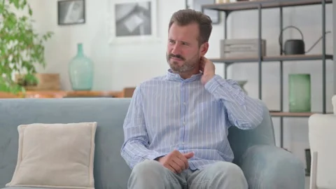 Middle Aged Man with Neck Pain Sitting on Sofa at Home Video stock 287897654