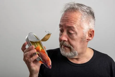Middle-aged man opens a can of canned fish from which a live fish comes out Stock Photos
