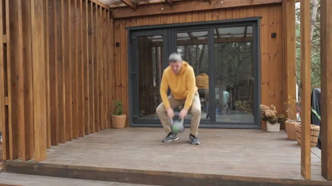 Middle aged man performing kettlebell squat on wooden terrace Stock Footage 324556816