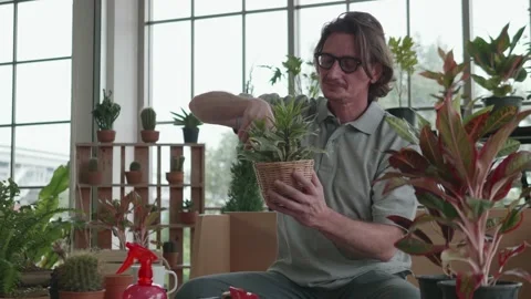 A middle-aged man is planting trees in the living room at home. Stock Footage 140033764