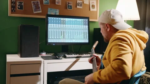 Middle-aged man playing guitar and creating music using equalizer program. Male Stock Footage 144436587