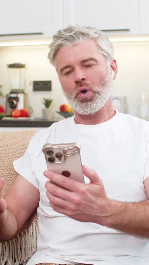Middle-aged man practices language phrases with headphones on smartphone app Stock Footage 347615837
