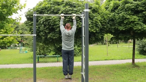 A middle-aged man pulls himself up on a horizontal bar in an autumn park Stock Footage 141261746