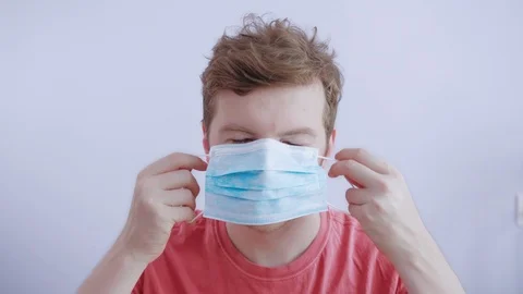 Middle-aged man puts on a protective medical mask in white studio to be safe Video stock 126421592