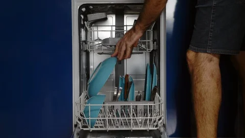 Middle-aged man putting plates and glasses in the dishwasher Stock Footage 128820573