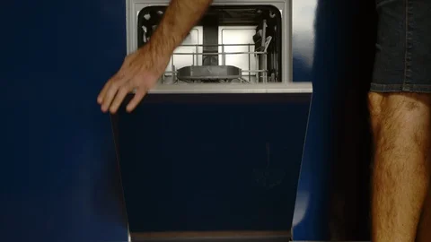 Middle-aged man putting plates and glasses in the dishwasher Stock Footage 128821352