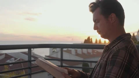 Middle aged man reading book on sunset, freelancer on balcony read during home Stock Footage 143648393