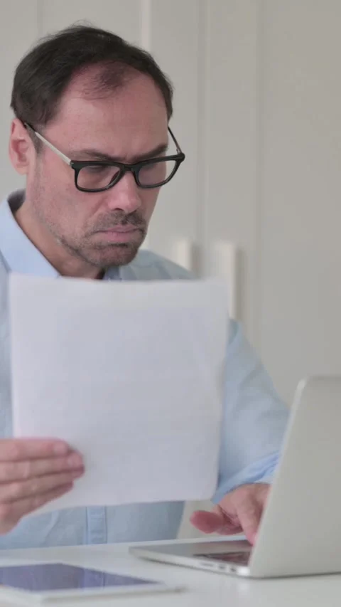 Middle Aged Man Reading Documents while using Laptop, Vertical Video 스톡 동영상 339584778