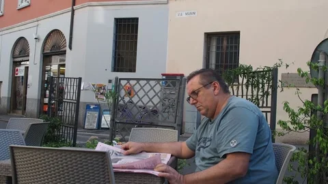 Middle aged man reading newspaper, wearing glasses, sitting at outdoor cafe.. Stock Footage 312981644
