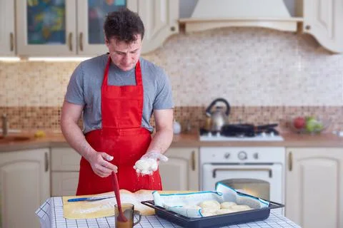 A middle-aged man in a red apron makes dough pies at home in the kitchen Stock Photos