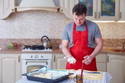 A middle-aged man in a red apron makes dough pies at home in the kitchen Stock Photos