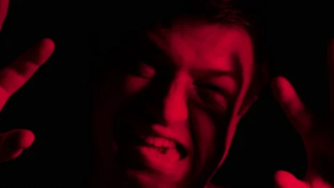 A middle-aged man in a red light, making scary faces Stock Footage 141818114