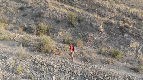 A middle-aged man in a red shirt and shorts, with trekking poles and a back.. Video stock 283723135