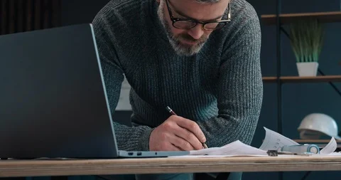 Middle Aged man Redrawing blueprints on paper and looking at Laptop, Using Vídeo Stock 126244375