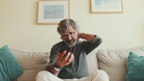Middle-aged man relaxing on his couch while using his smartphone Vídeo Stock 229506721