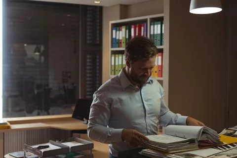 Middle aged man reviewing documents at office workspace with large binder and Stock Photos