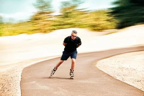 Middle-aged man rides inline skates on an asphalt track Stock Photos