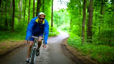 Middle-aged man is riding a road bike along a forest road Video stock 78420058