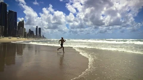 A middle-aged man runs joyfully along the shoreline at Gold Coast beach, kicking Stock Footage 306124272