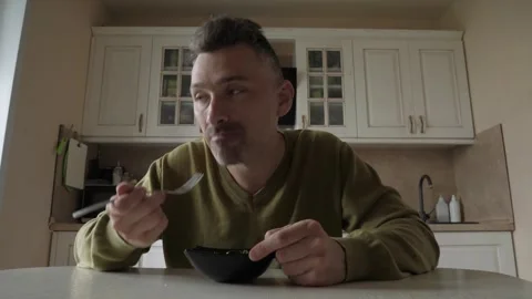 Middle-aged man seated at kitchen table eating cereal from ceramic bowl Stock Footage 341832861