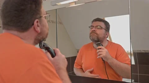 Middle aged man shaving with electric razor looking at bathroom mirror. Stock Footage 167281359