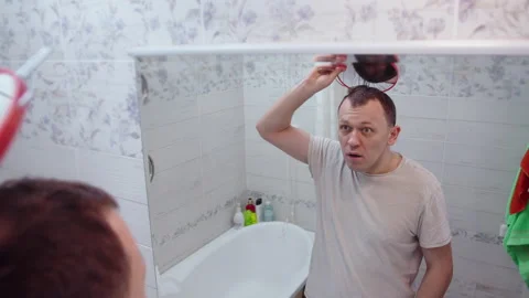 Middle-aged man is shocked to see the reflection of his bald head in the mirror Stock Footage 132822355