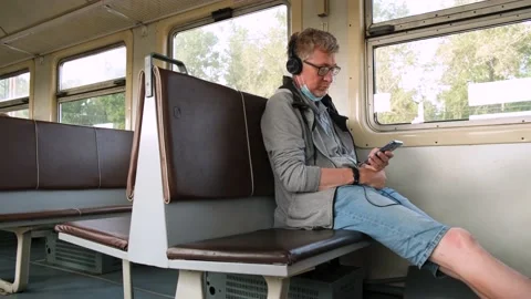 Middle-aged man is siting on public transport with headphones and using phone. Stock Footage 163498978