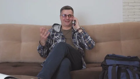 A middle-aged man sits on a couch in a hotel room and is talking on the phone Stock Footage 104586613