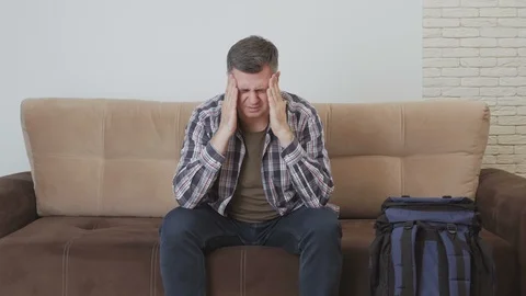 A middle aged man sits on a couch and holds his hands over his head, suffering Stock Footage 104789464