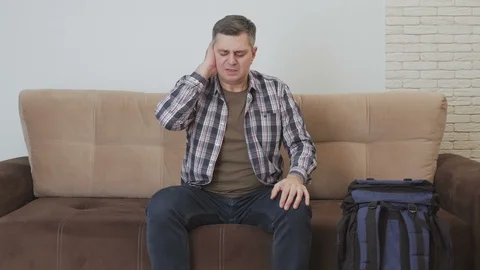 A middle aged man sits on a couch and suffers from earache. Next to the sofa is Stock Footage 104795606