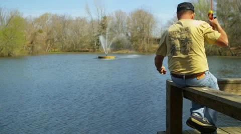 A middle-aged man sits on a dock fishing Stock Footage 22346268
