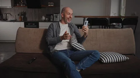 A middle-aged man sits in his living room, having a video call using his Stock Footage 297050471