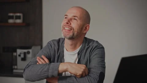 A middle-aged man sits at home, lost in thought, with a dreamy expression on his Video stock 295360132