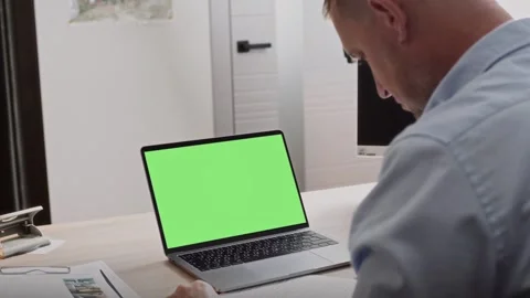 Middle-aged man sits in office behind a laptop with a green screen Stock Footage 307598597