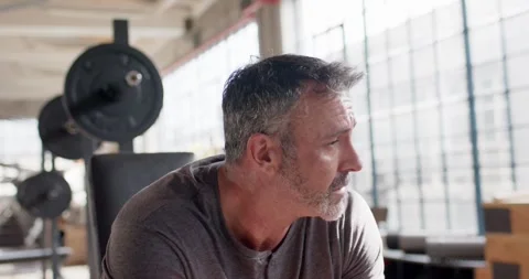 Middle-aged man sitting on bench by barbell in gym loft, hearing off-camera cue, Stock Footage 337289217