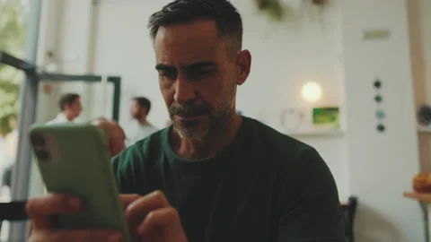 Middle-aged man sitting in cafe typing message on mobile phone Stock Footage 250841722