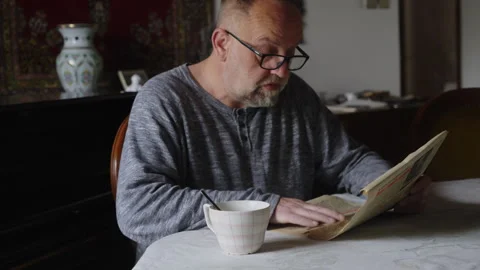 Middle Aged Man Sitting Comfortably at Home Reading Newspaper and Drinking Stock Footage 337764546