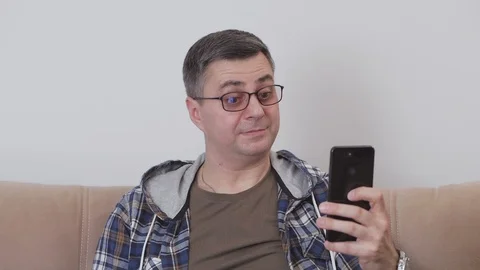 A middle-aged man, sitting on a couch, takes a picture of himself using a Stock Footage 104600499
