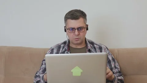 Middle-aged man sitting on the couch with a laptop emotionally grimacing looks Stock Footage 104786626